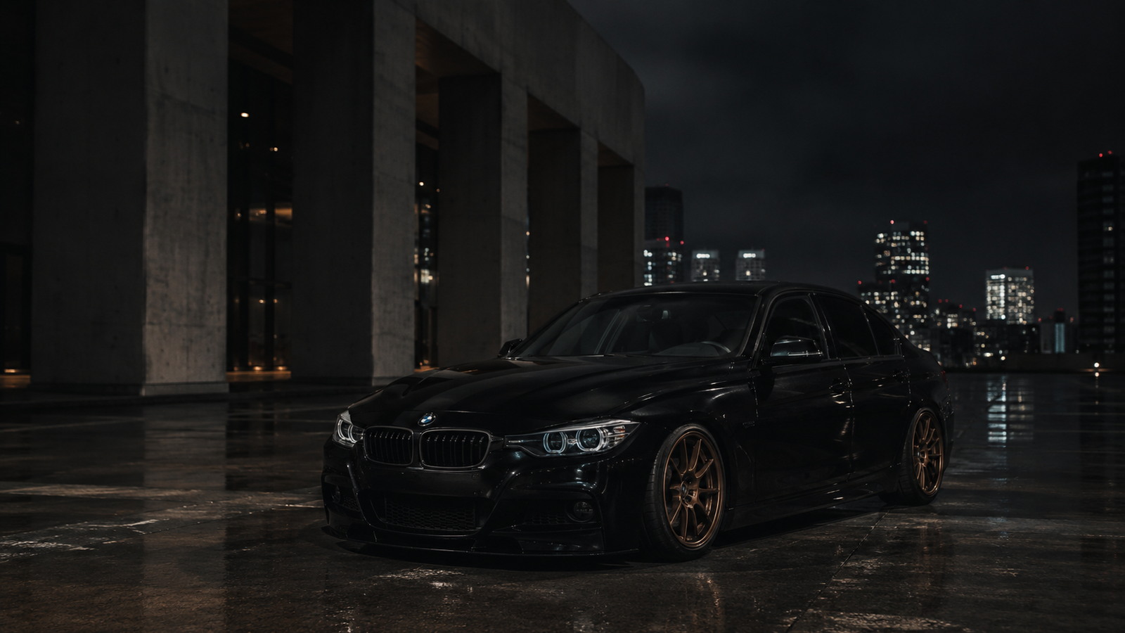 A black BMW F30 on wet pavement beneath city lights.