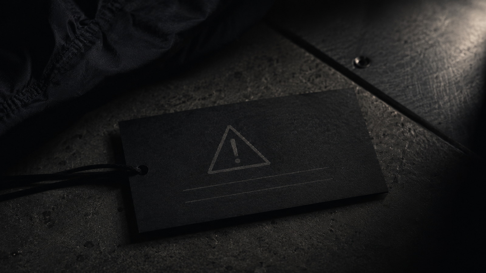 A black warning tag resting on an industrial surface under hard light.